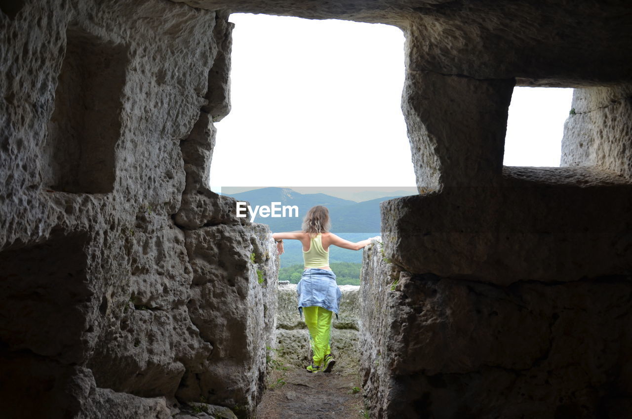 Portrait of young woman standing against stone wall