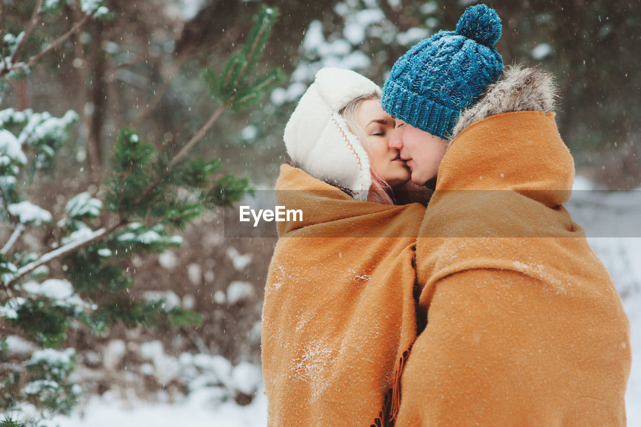 Woman kissing man while wearing warm clothing during winter