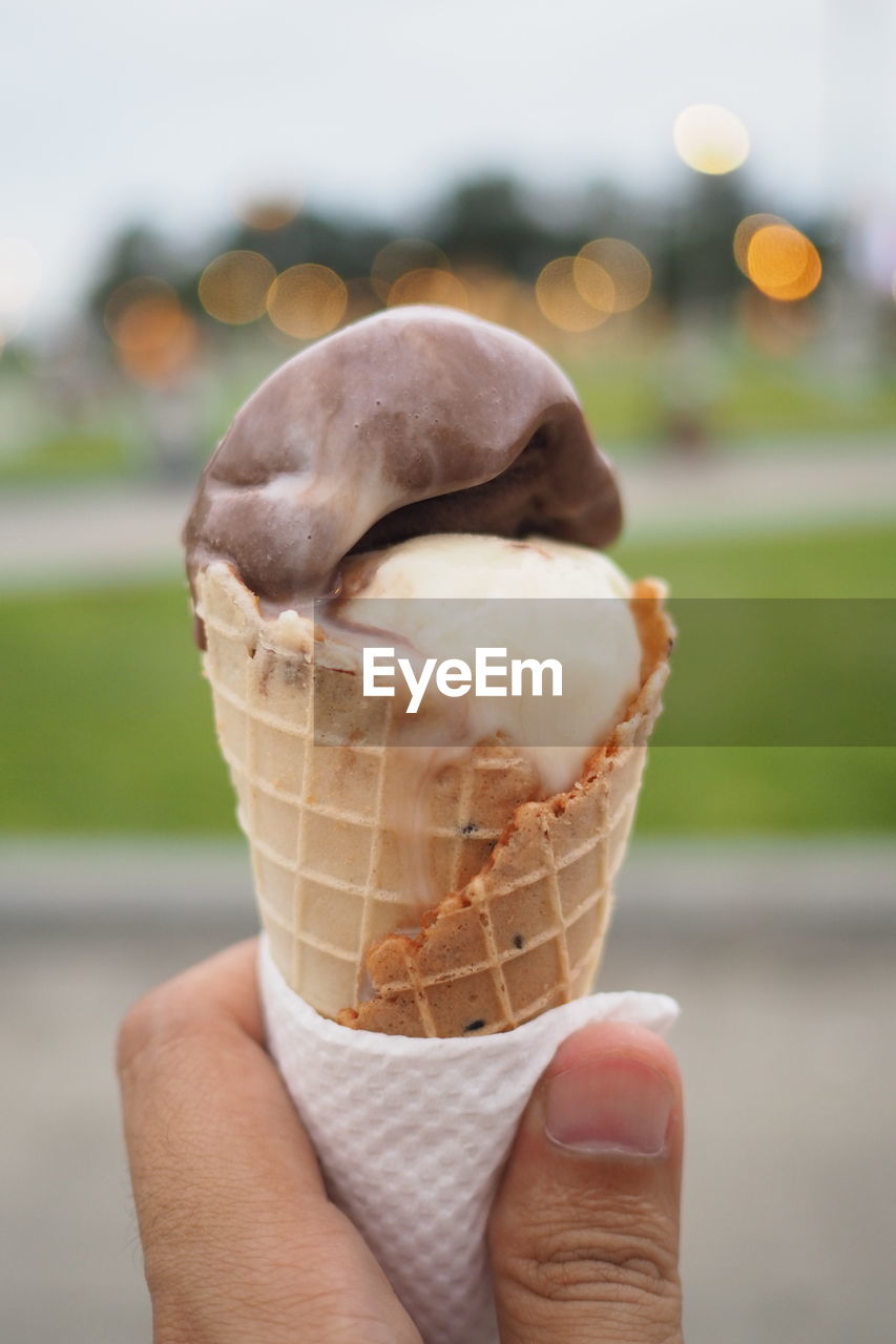 CLOSE-UP OF HAND HOLDING ICE CREAM CONE OUTDOORS