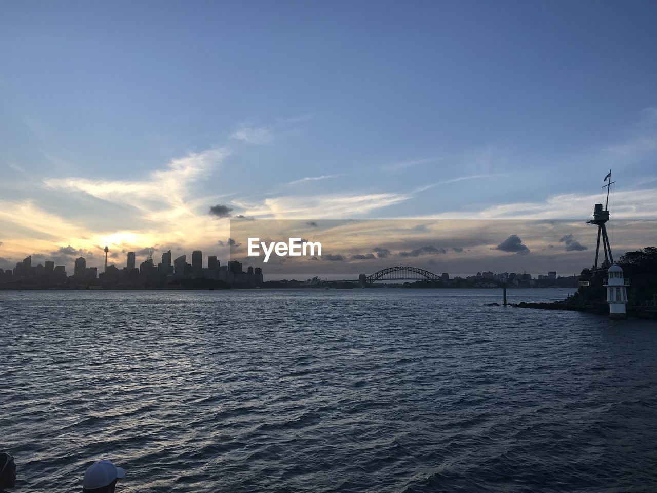 View of city at waterfront against cloudy sky