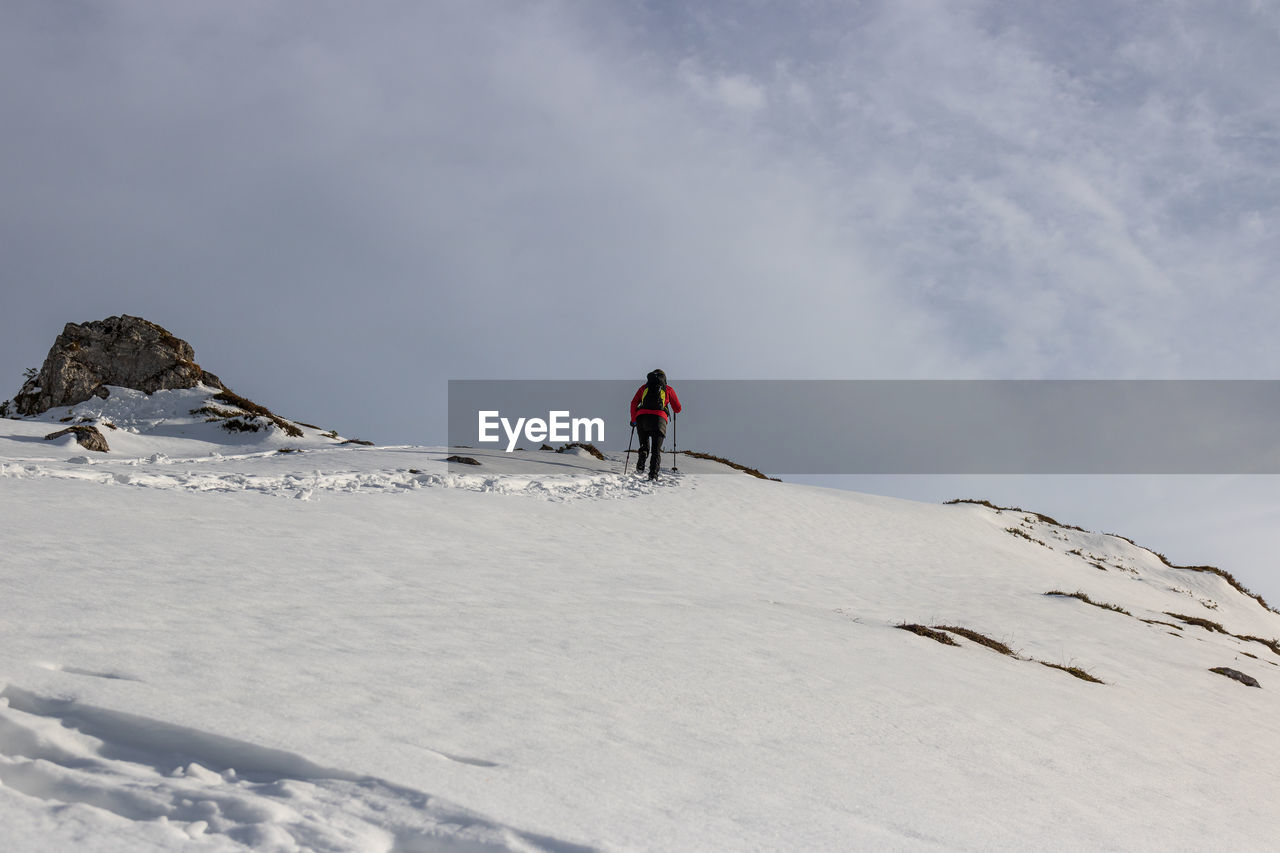 REAR VIEW OF PERSON SKIING ON SNOWCAPPED MOUNTAIN AGAINST SKY