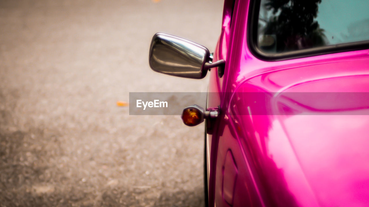 Side mirror and window of beautiful vintage pink car over blur background