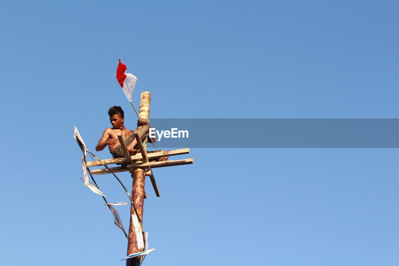 LOW ANGLE VIEW OF MEN ON BLUE AGAINST CLEAR SKY