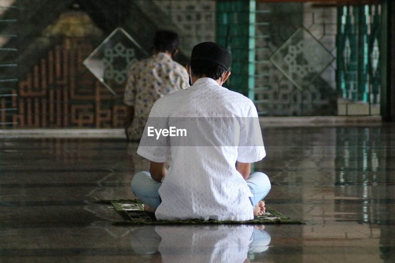 REAR VIEW OF MAN SITTING ON FLOOR IN GLASS