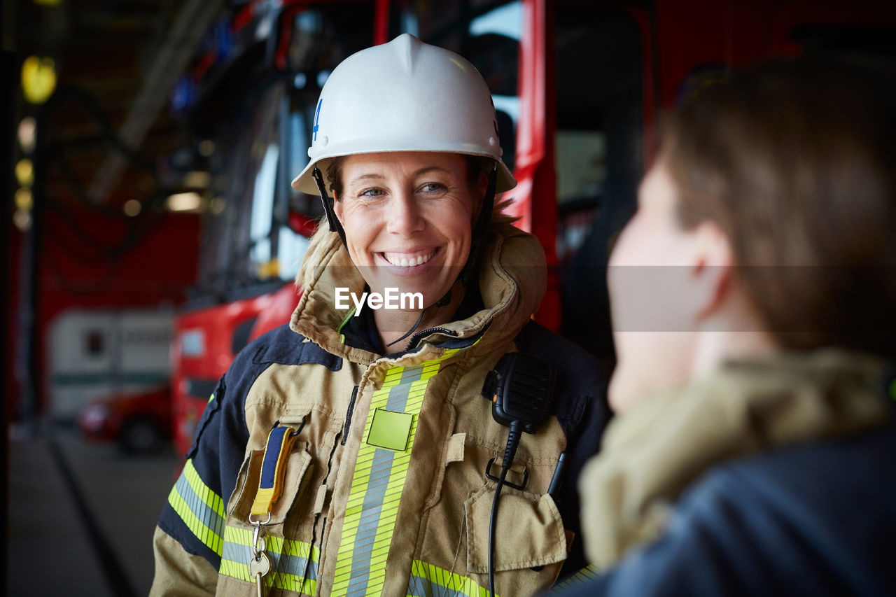 Smiling female firefighter looking at coworker in fire station