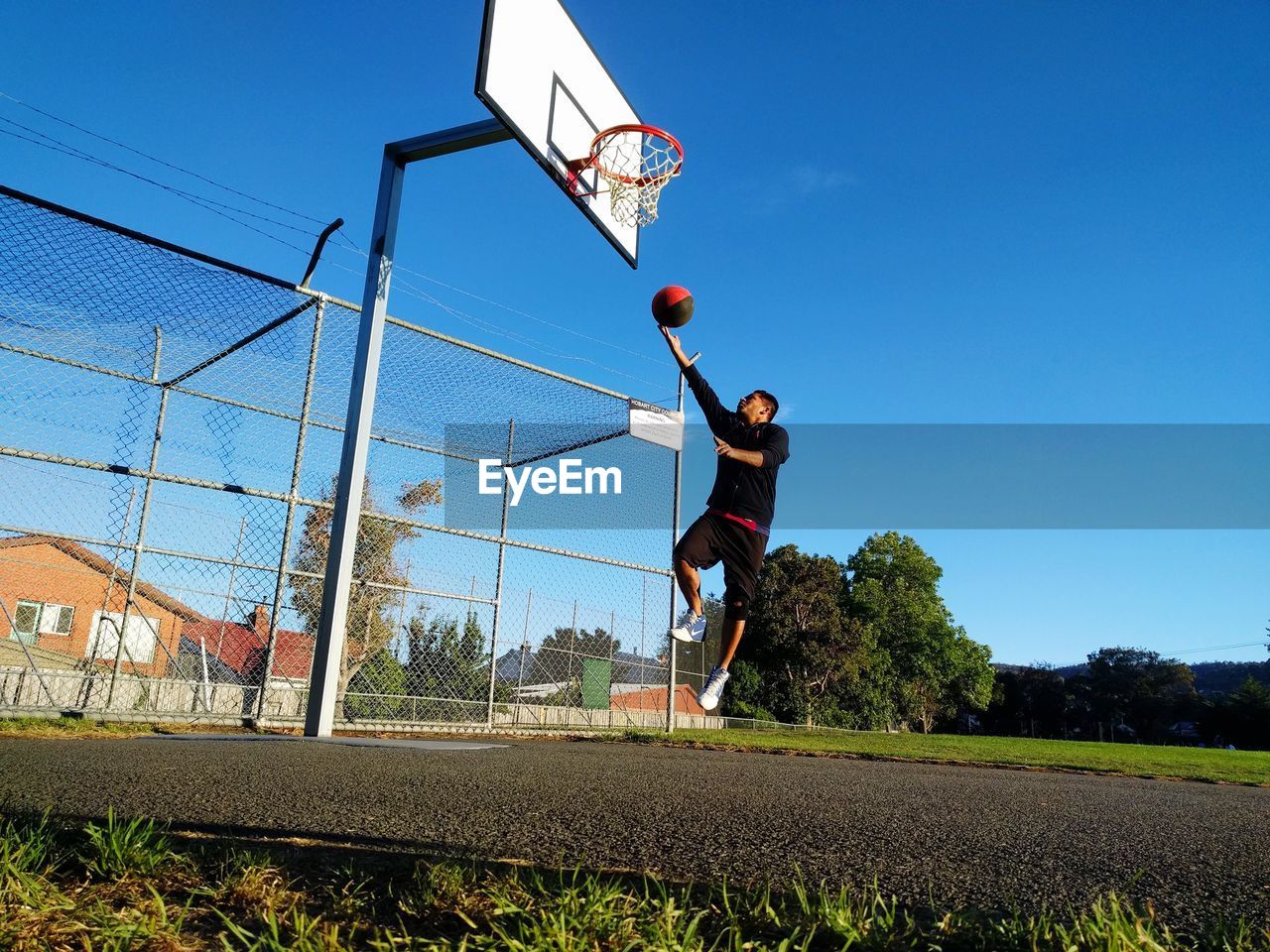 Low angle view of young man playing basketball against clear blue sky
