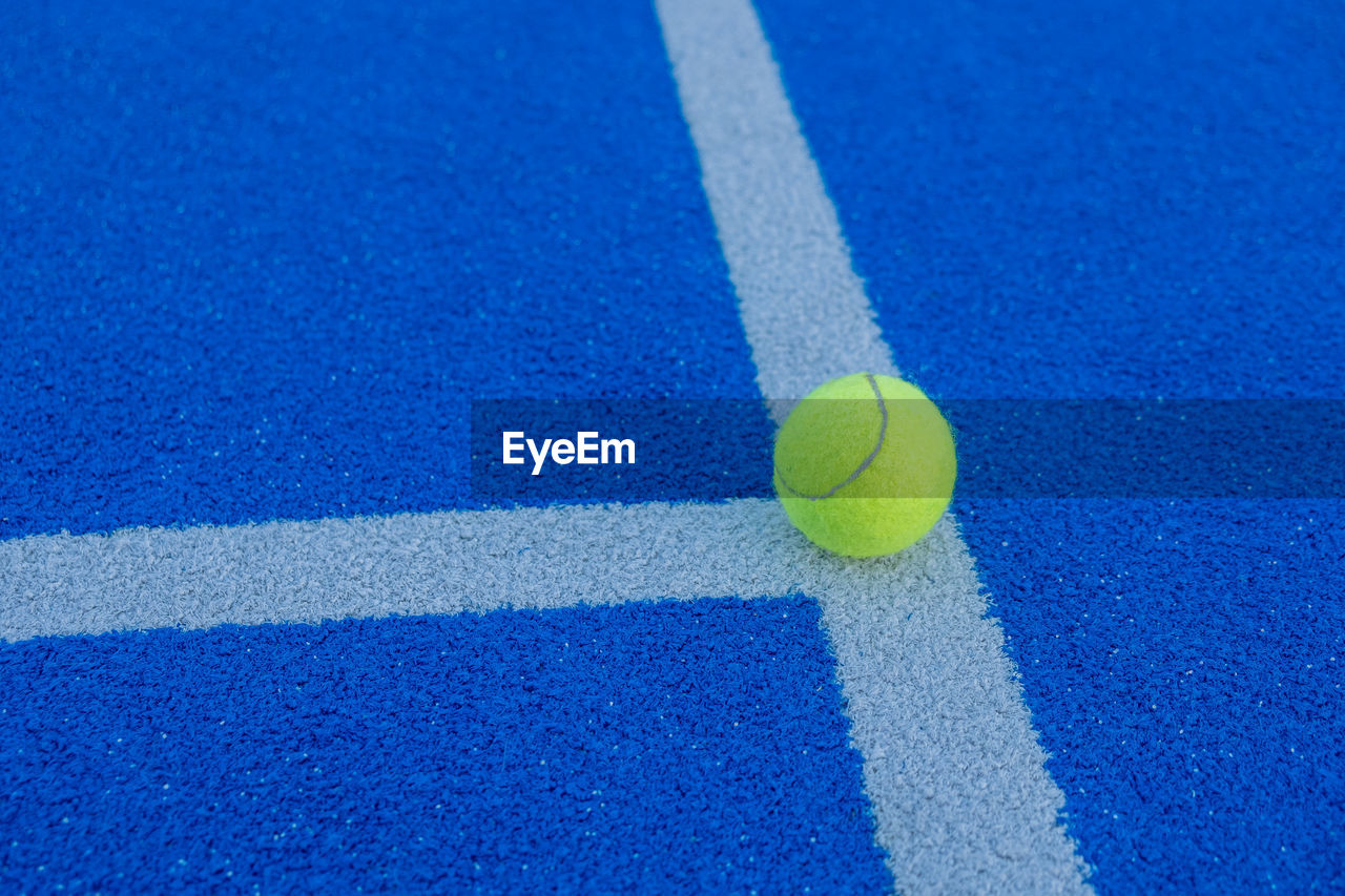 A ball on the line of a paddle tennis court of blue synthetic grass. health and sport concept