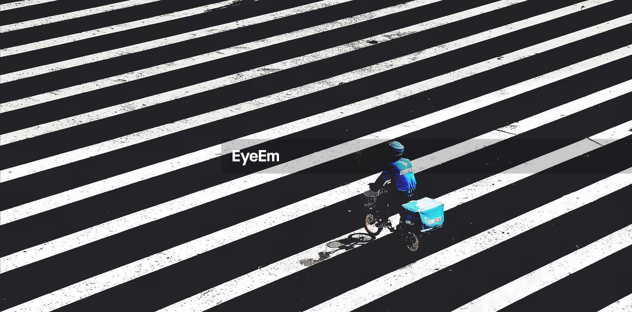 HIGH ANGLE VIEW OF MAN WALKING ON ZEBRA CROSSING IN CITY