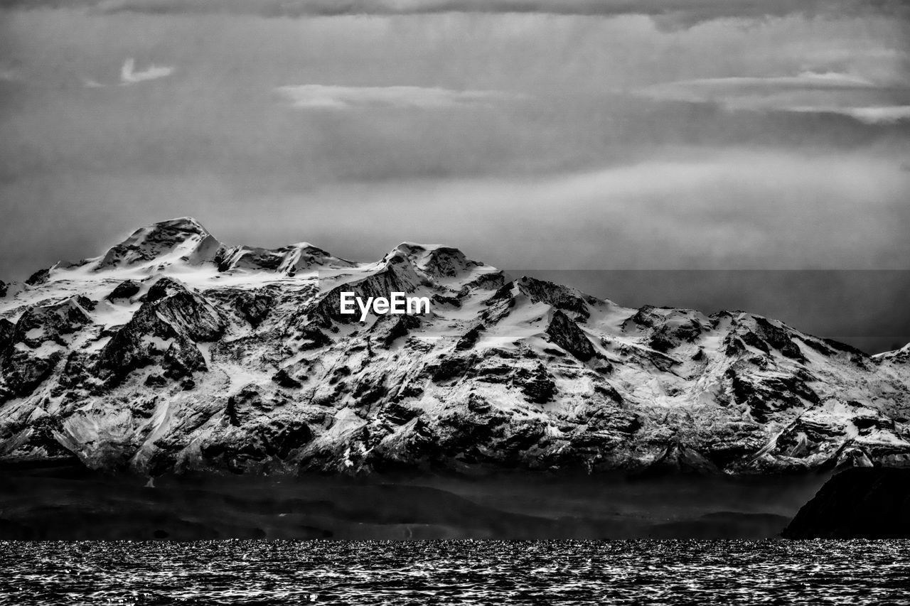 black and white, monochrome photography, monochrome, cloud, mountain, snow, environment, rock, nature, wave, scenics - nature, beauty in nature, darkness, cold temperature, landscape, water, sea, sky, winter, no people, ocean, horizon, land, white, black, coast, tranquility, outdoors, snowcapped mountain, mountain range, non-urban scene, travel destinations, tranquil scene, day, extreme terrain, glacier, travel, ice