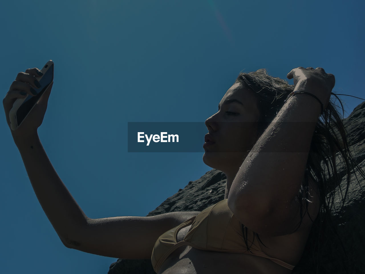 Low angle view of woman photographing against blue sky