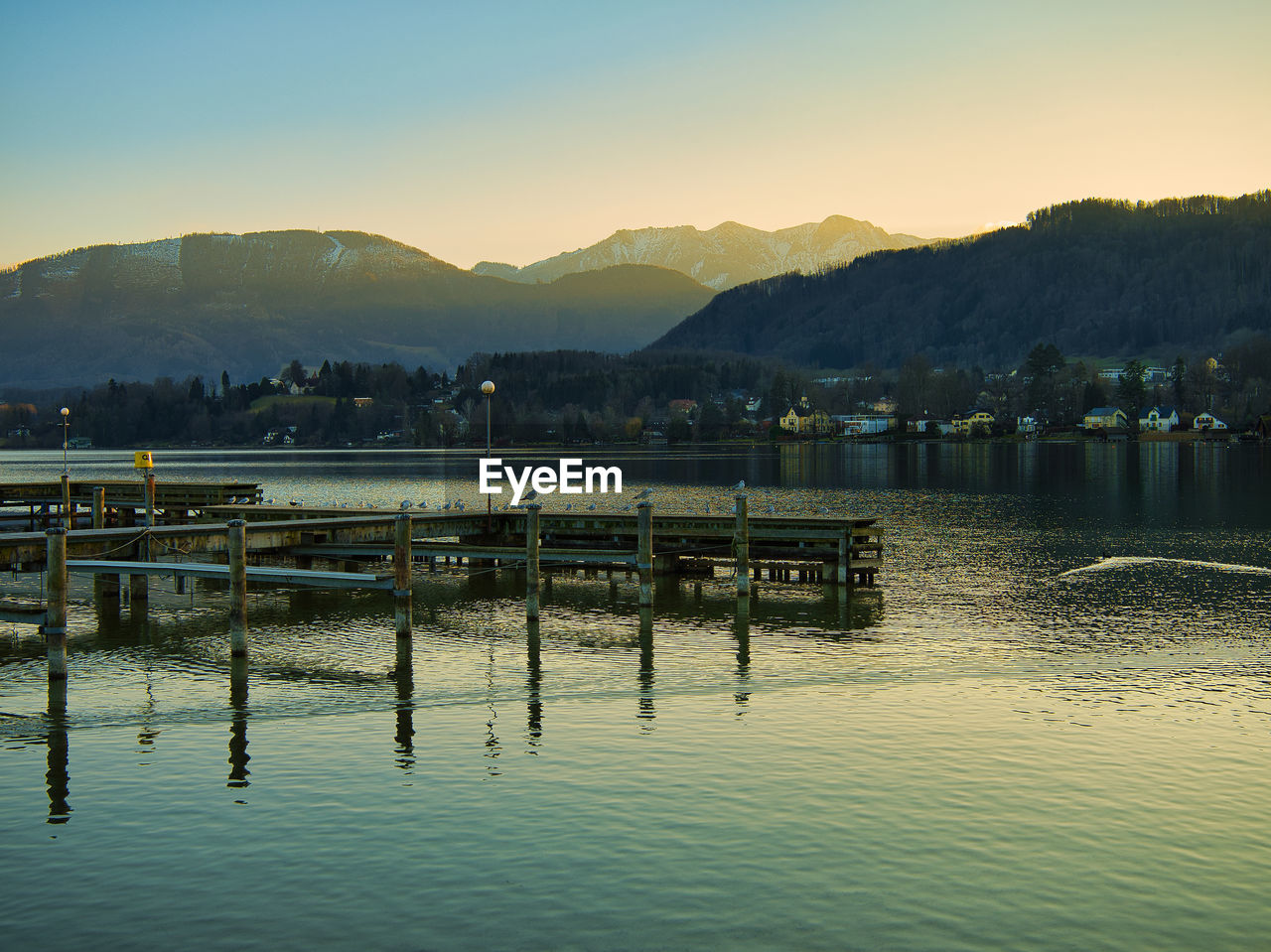 PIER OVER LAKE AGAINST MOUNTAINS DURING SUNSET