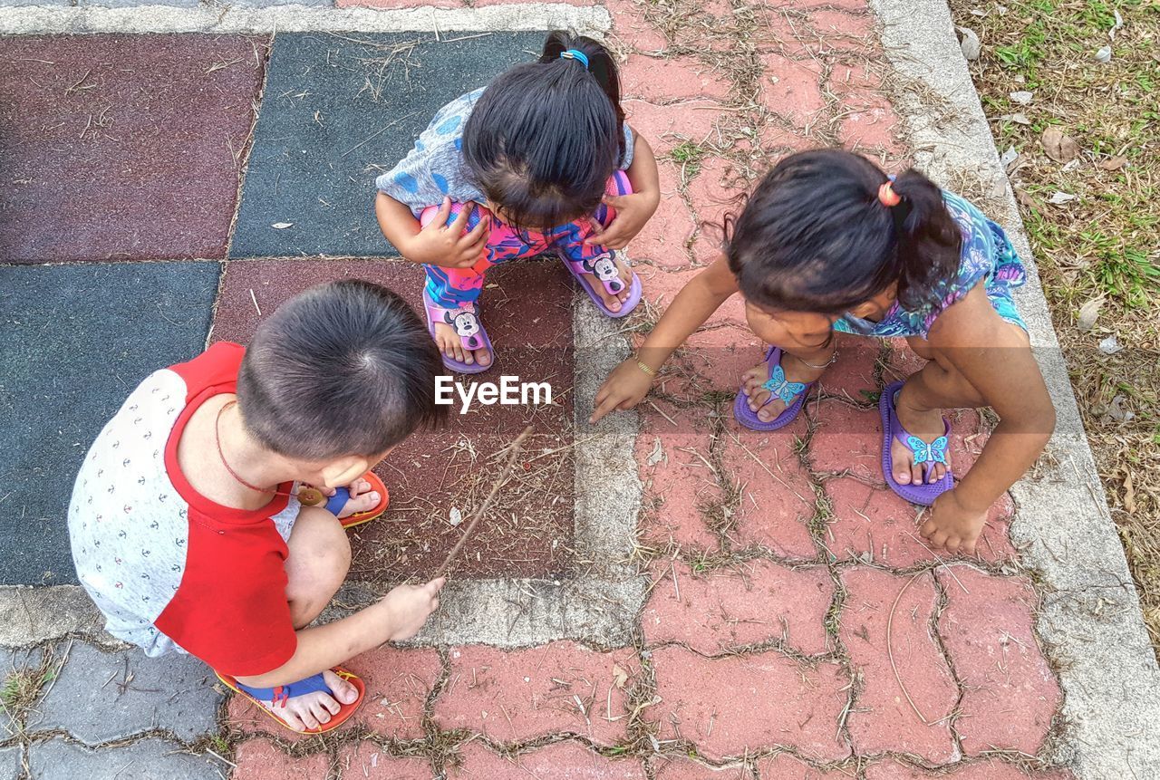 HIGH ANGLE VIEW OF CHILDREN ON MULTI COLORED COBBLESTONE