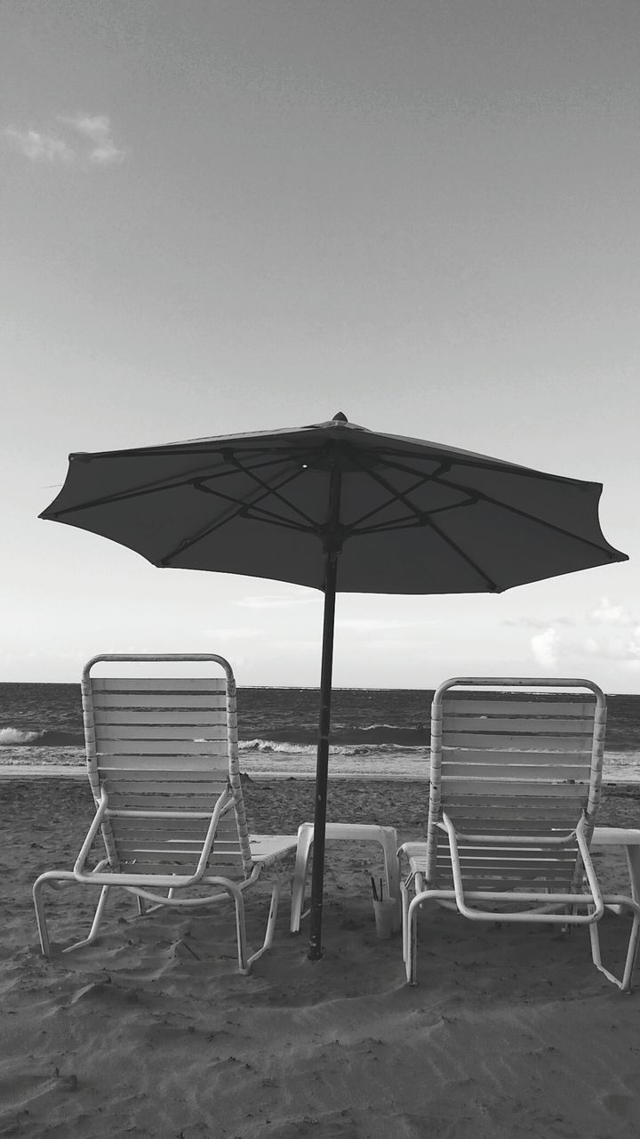 Empty chairs and parasol at beach against sky