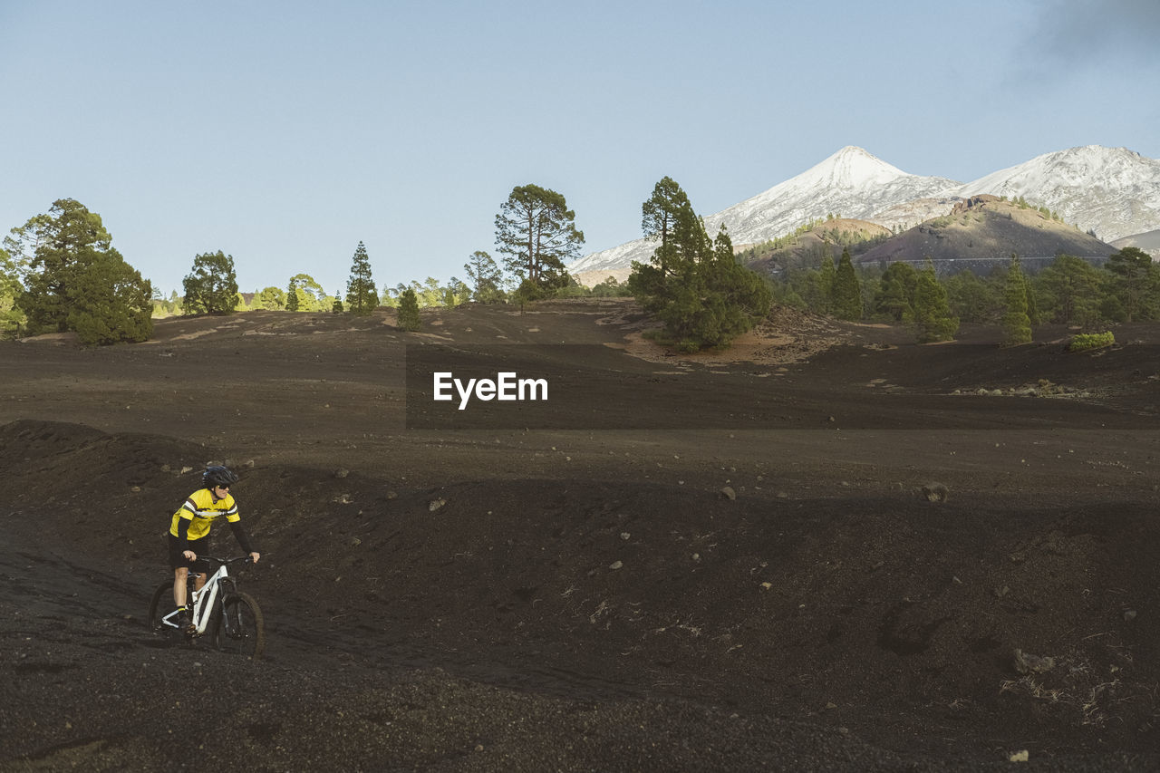 Female cyclist riding on dirt track with snowy mount teide in back