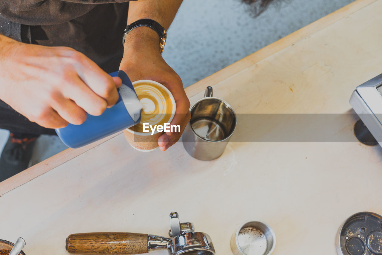 Cropped image of hand making froth art in espresso coffee at counter in cafe