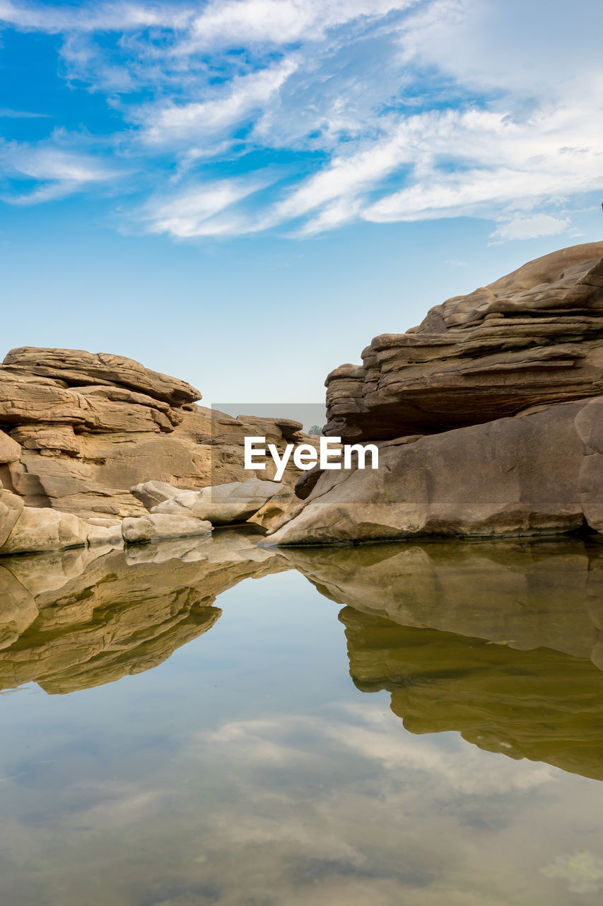 SCENIC VIEW OF ROCK FORMATION BY LAKE AGAINST SKY