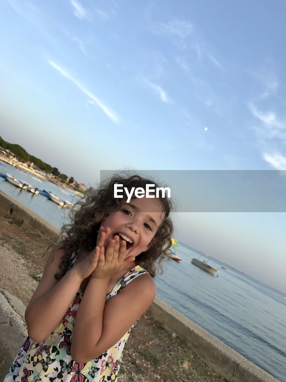 water, vacation, one person, sea, sky, beach, women, land, smiling, nature, blue, happiness, emotion, holiday, leisure activity, trip, child, portrait, hairstyle, female, childhood, summer, photo shoot, adult, cloud, person, cheerful, young adult, day, long hair, enjoyment, horizon over water, brown hair, outdoors, horizon, ocean, lifestyles, front view, clothing, relaxation, swimwear, sand, fun, dress, smile, teeth, looking, sunlight, beauty in nature, casual clothing, eyes closed, waist up, carefree, looking at camera