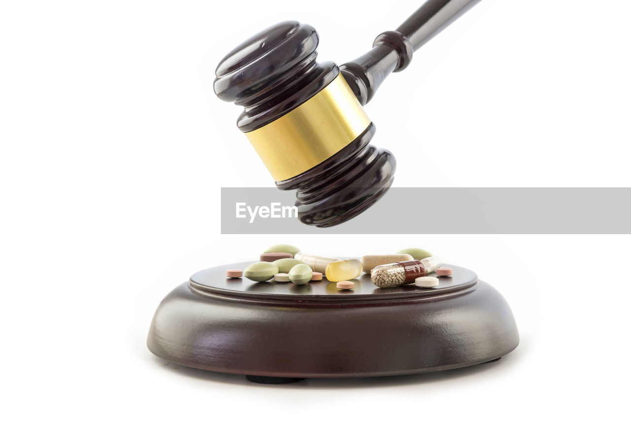 Close-up of gavel and medicines over white background