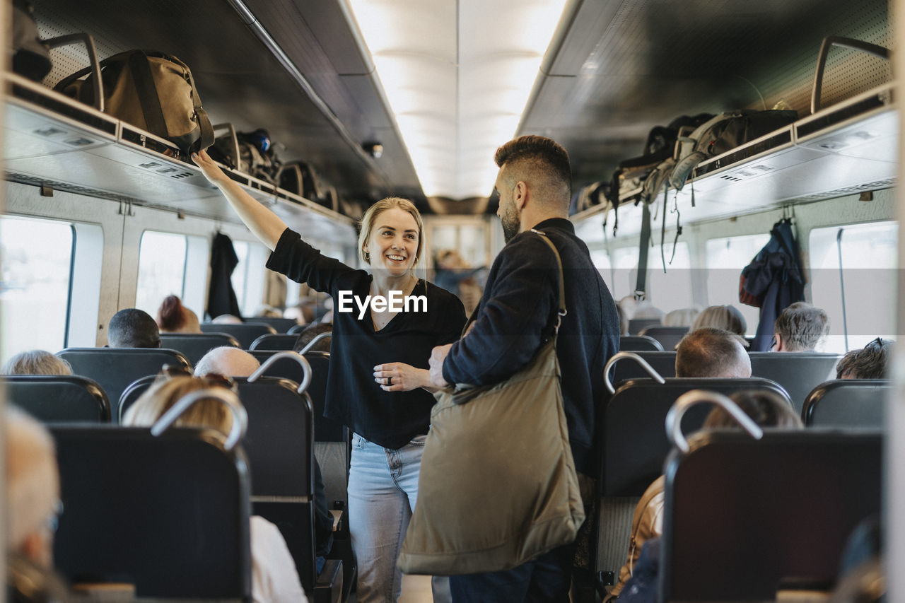 Smiling woman talking to man while standing between seats in train