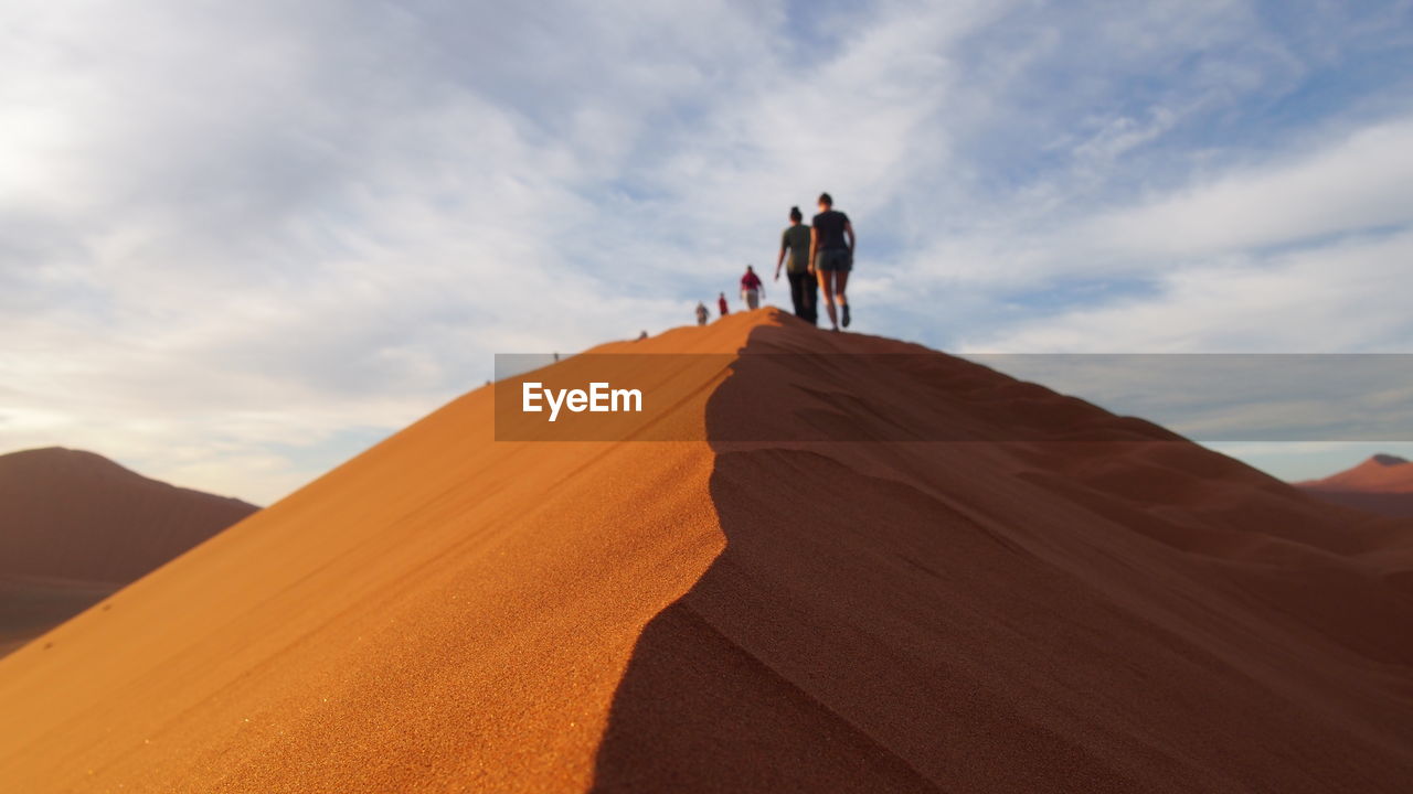 Rear view of people walking on desert against sky
