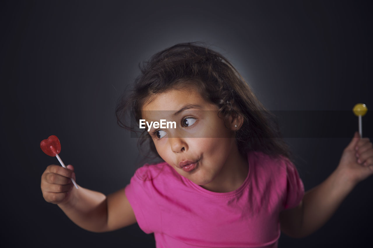 Girl holding candies while standing against black background