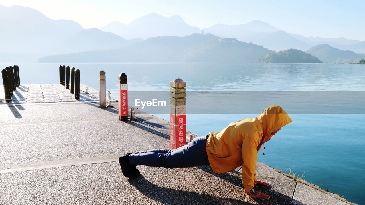 MAN STANDING ON SEA AGAINST MOUNTAINS