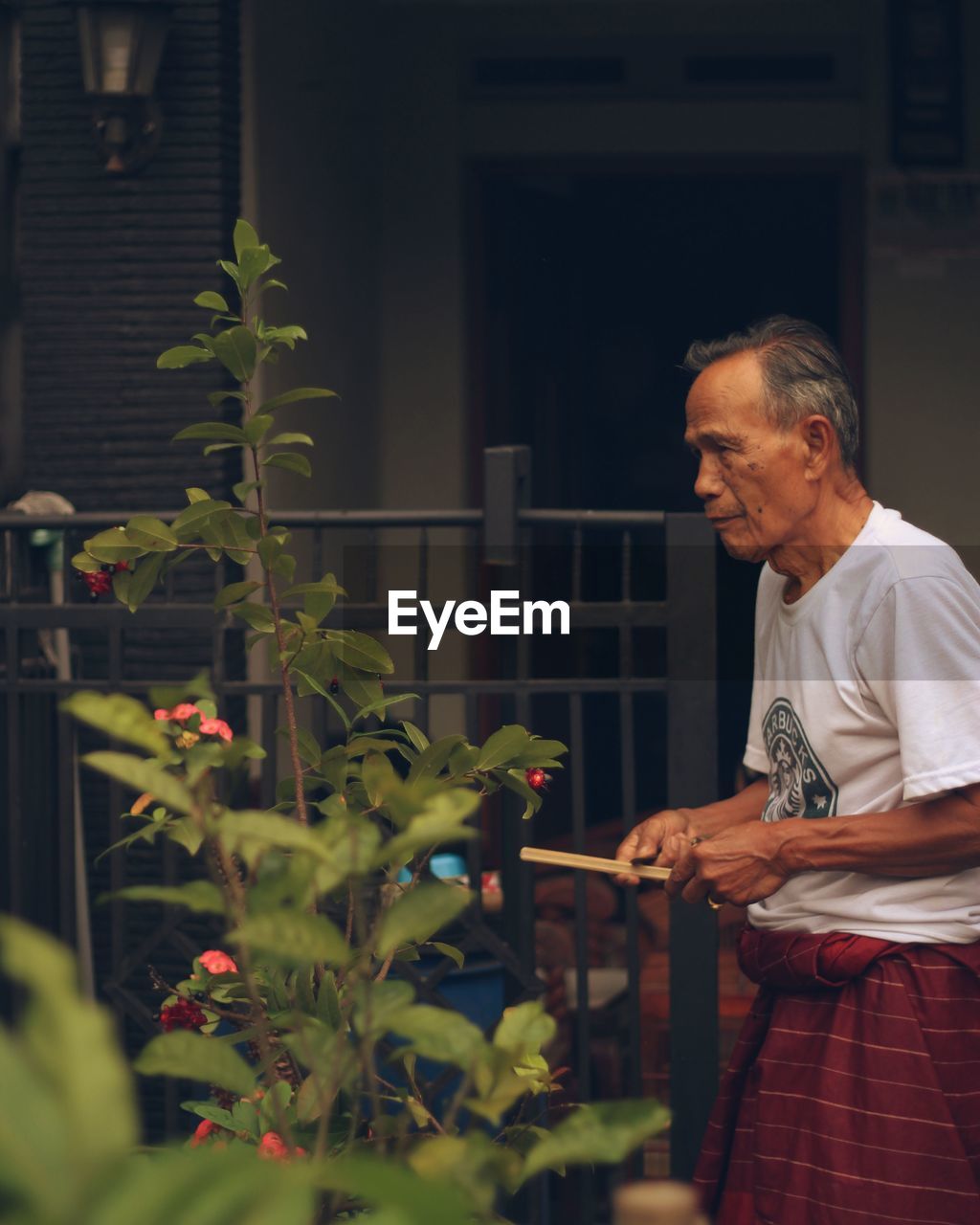 Senior man standing by plant against fence in yard