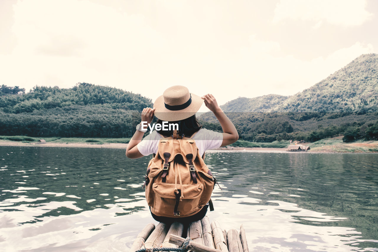 Rear view of woman sitting by lake on wooden raft