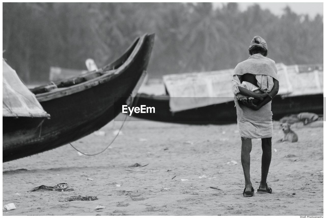 Rear view of man walking by boats at beach