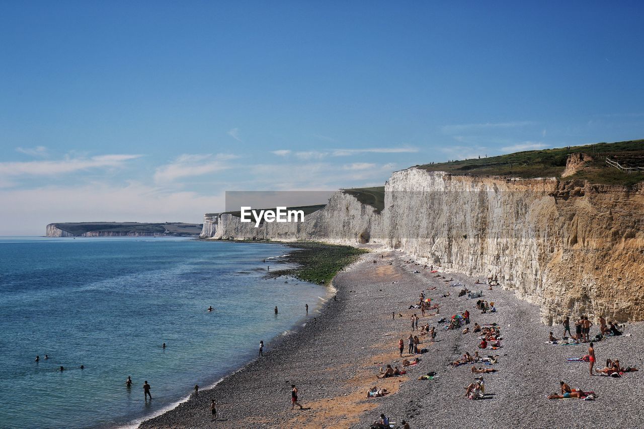 PANORAMIC VIEW OF PEOPLE ON BEACH AGAINST BLUE SKY
