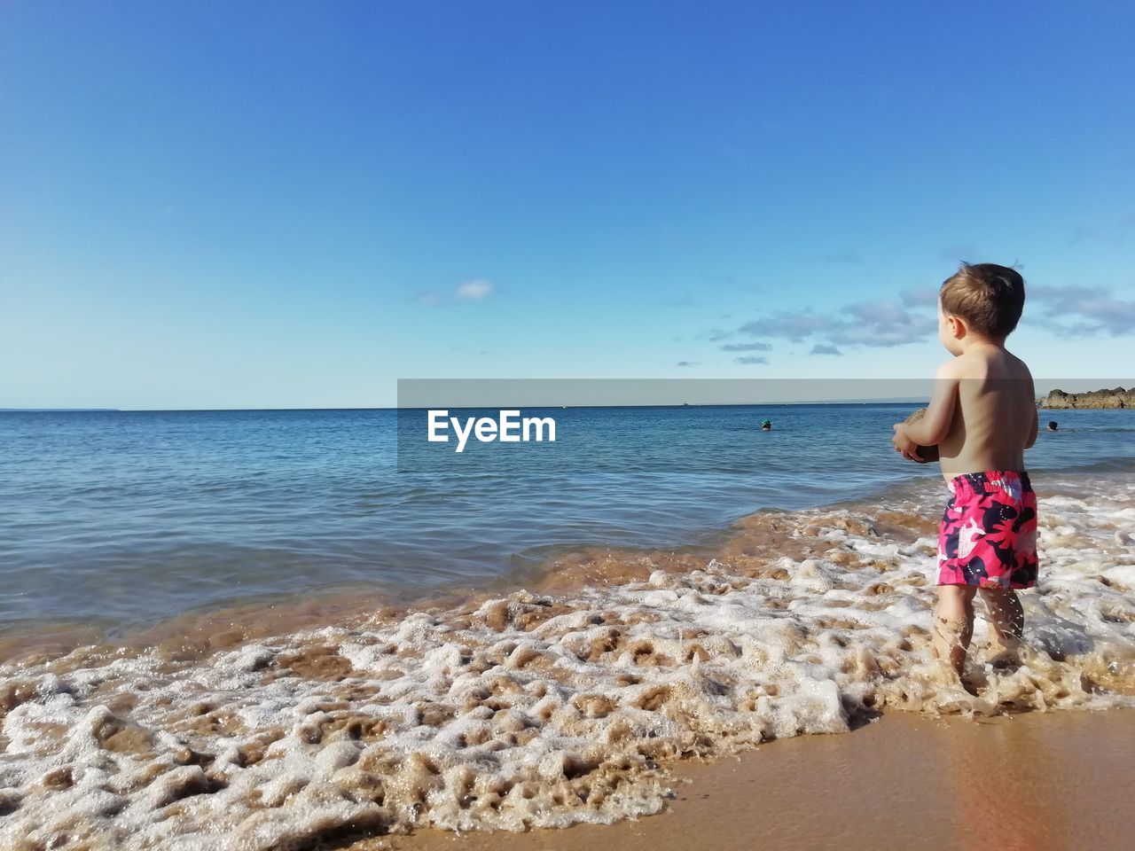 Full length of shirtless boy on beach against sky