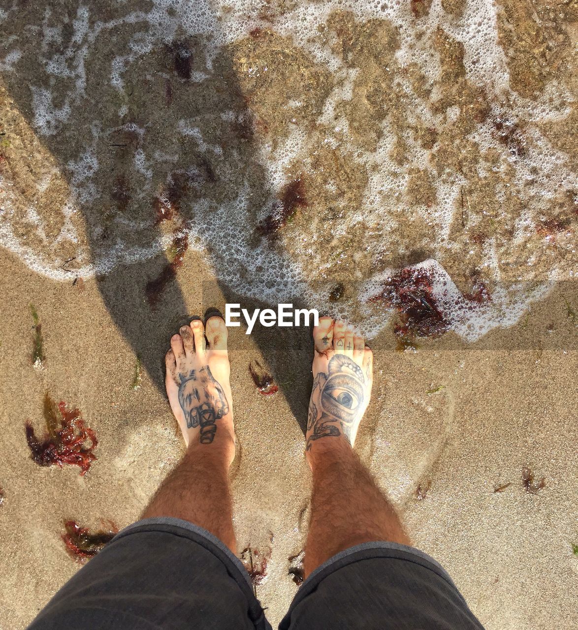 LOW SECTION OF PERSON STANDING ON SAND