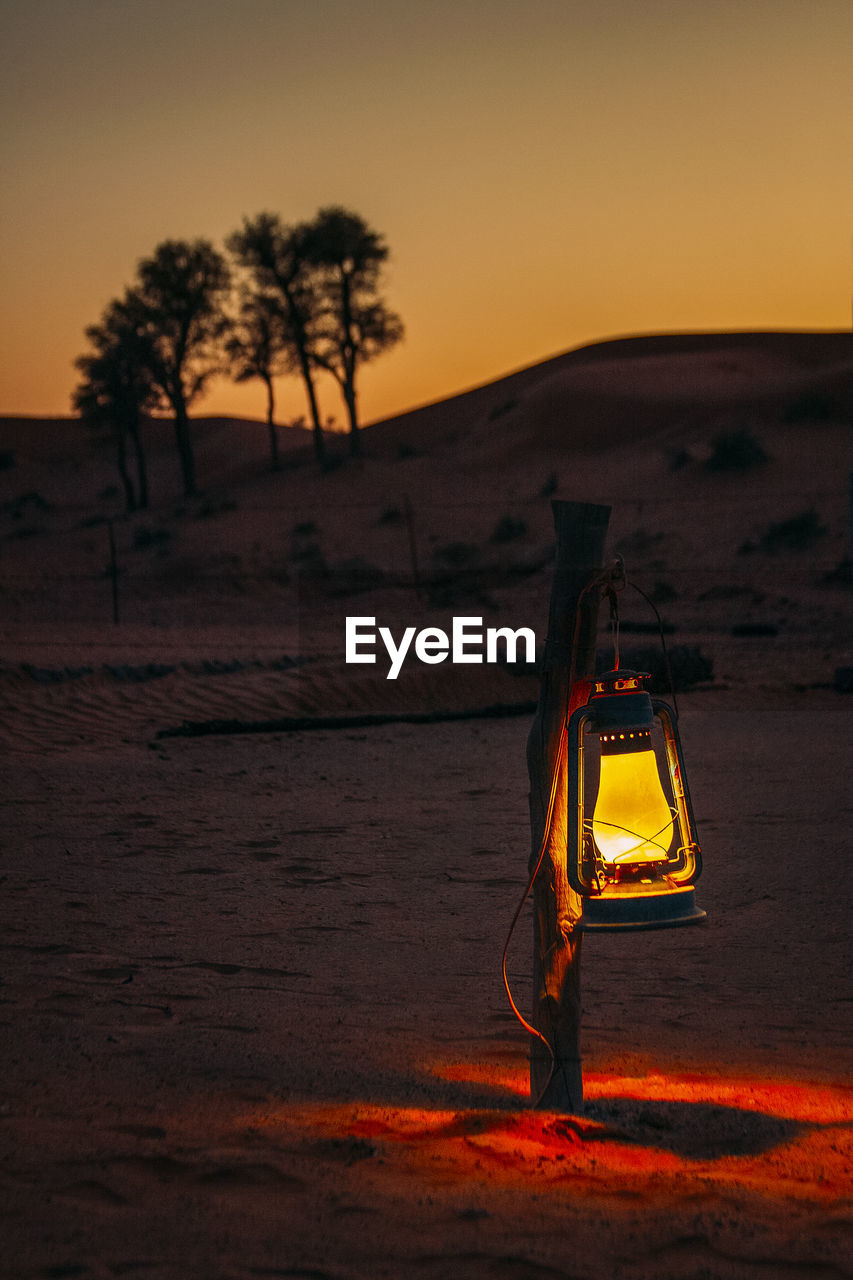 Lantern hanging on wooden post during sunset