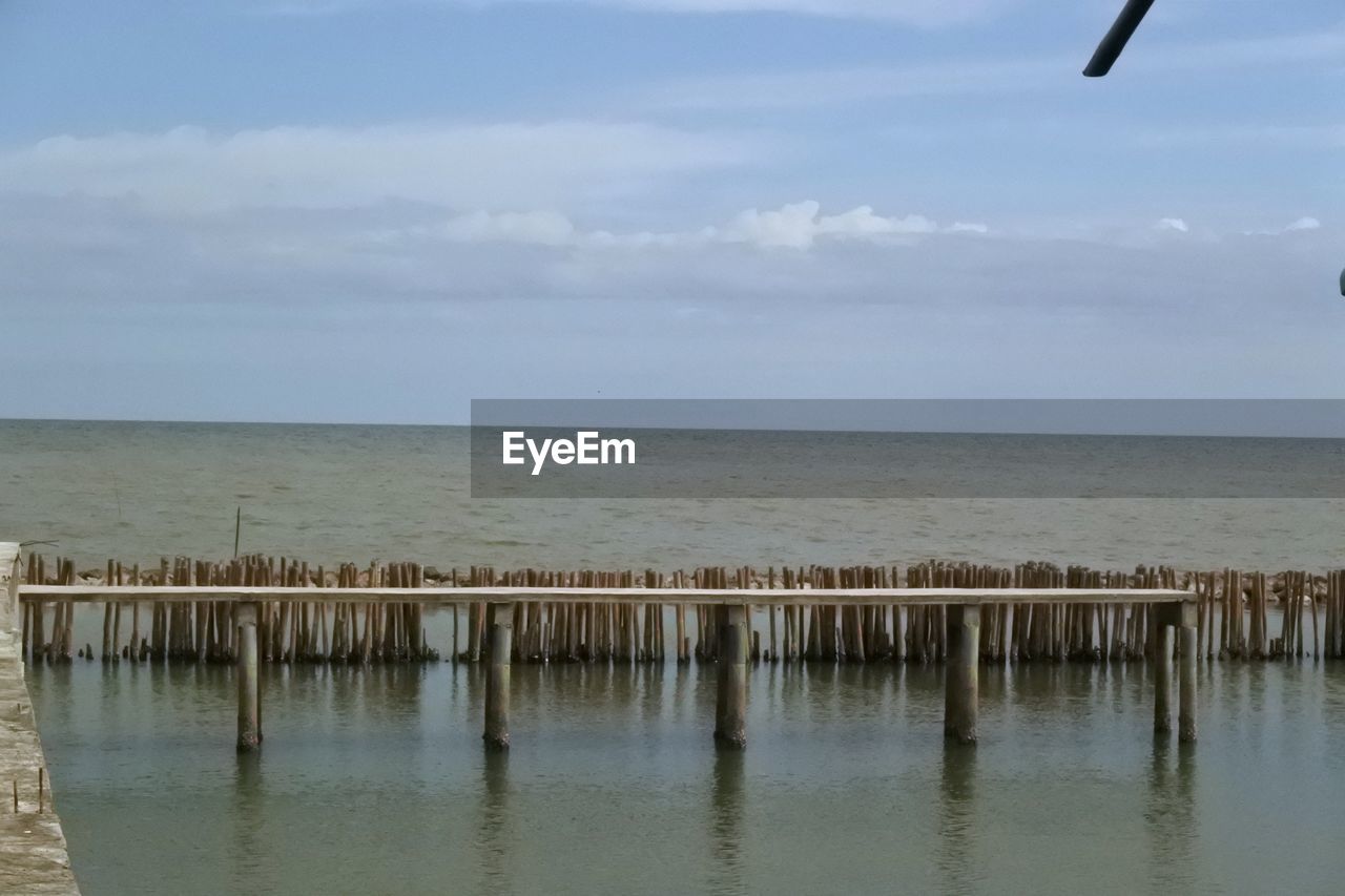 WOODEN POSTS ON BEACH AGAINST SKY