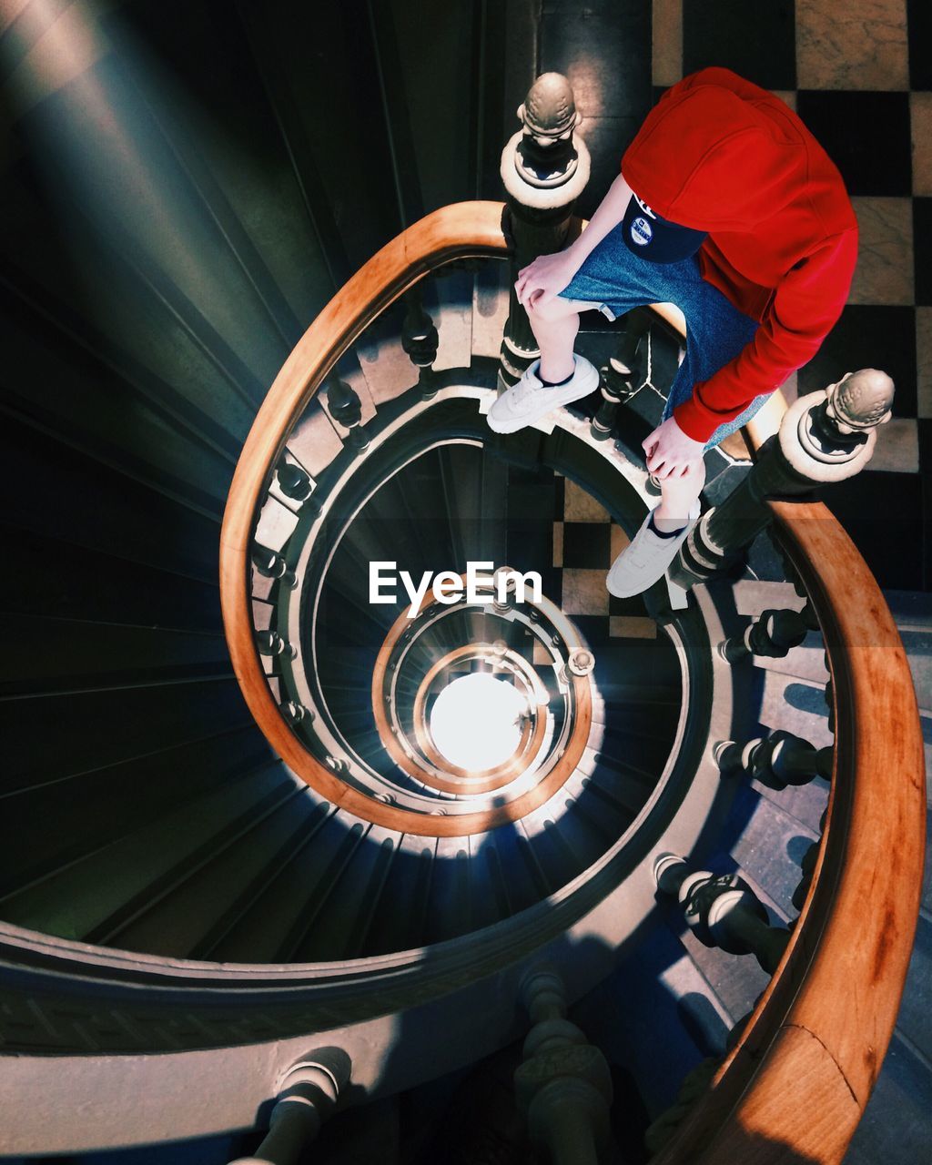 High angle view of man in red hooded short sitting on spiral steps railing