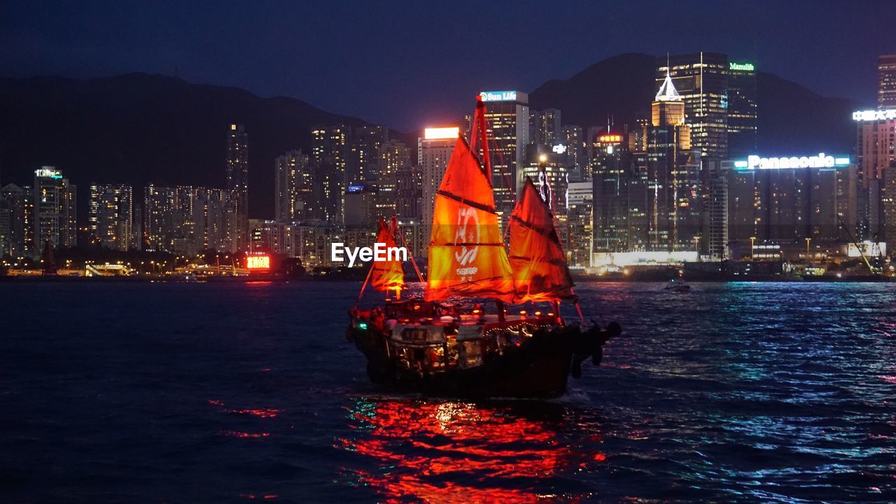 ILLUMINATED MODERN BUILDINGS BY SEA AGAINST SKY AT NIGHT