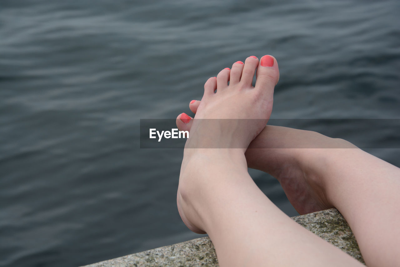 Low section of woman relaxing on pier by lake