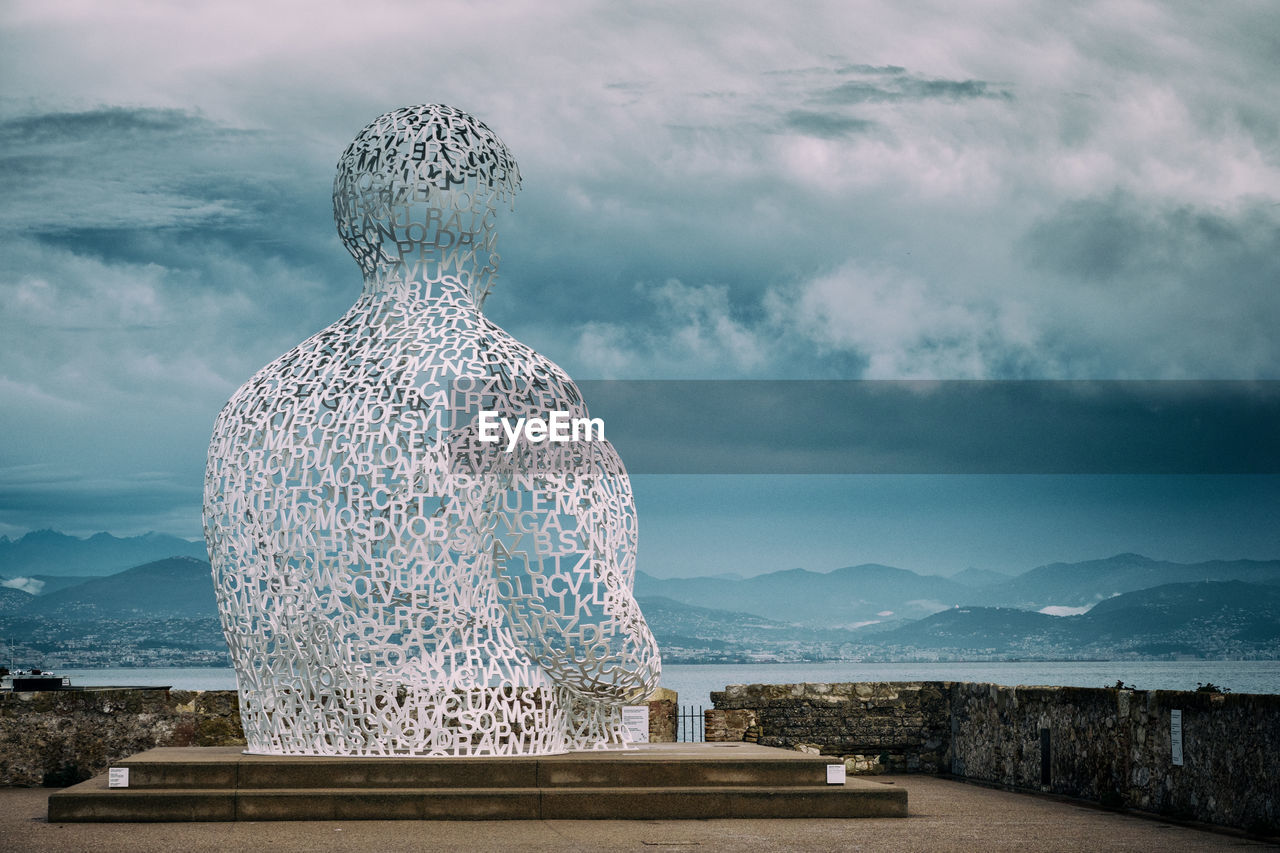 Statue of a contemplating man  made up entirely of letters looking out on sea and mountains