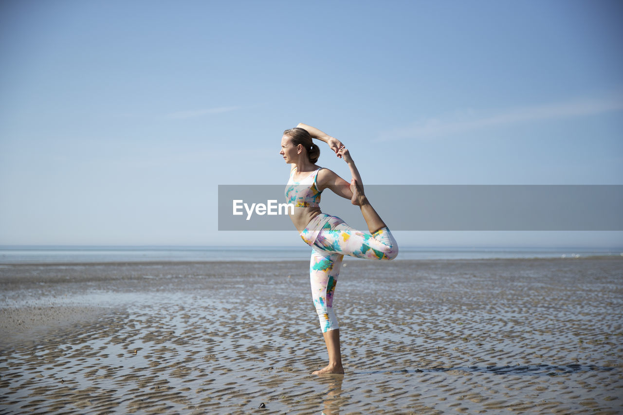 Woman exercising at beach against sky