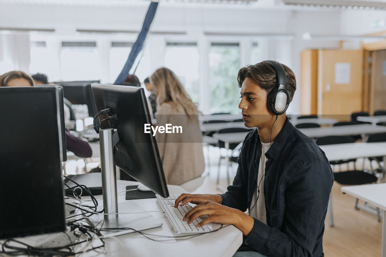 Teenage boy listening through headphones while using computer in school lab