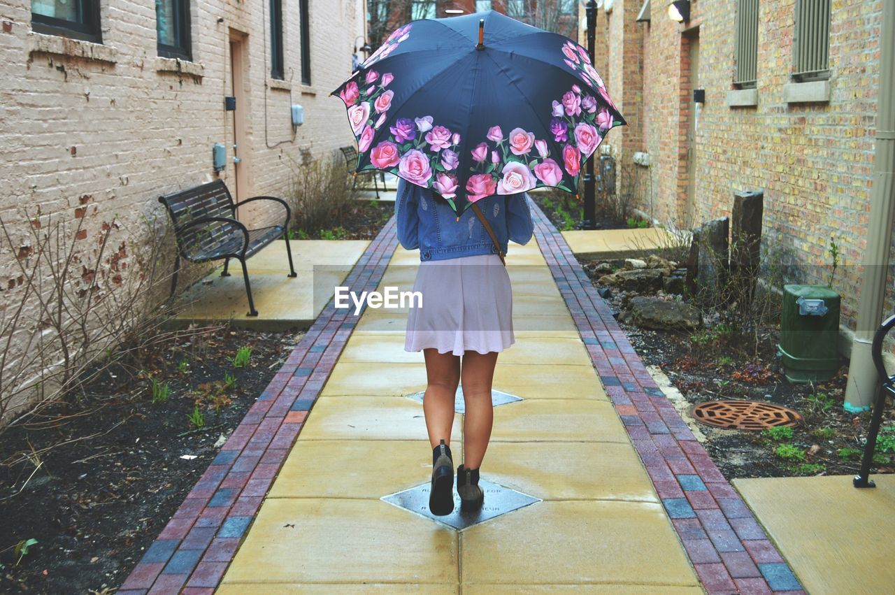 Rear view of fashionable women wearing skirt holding umbrella