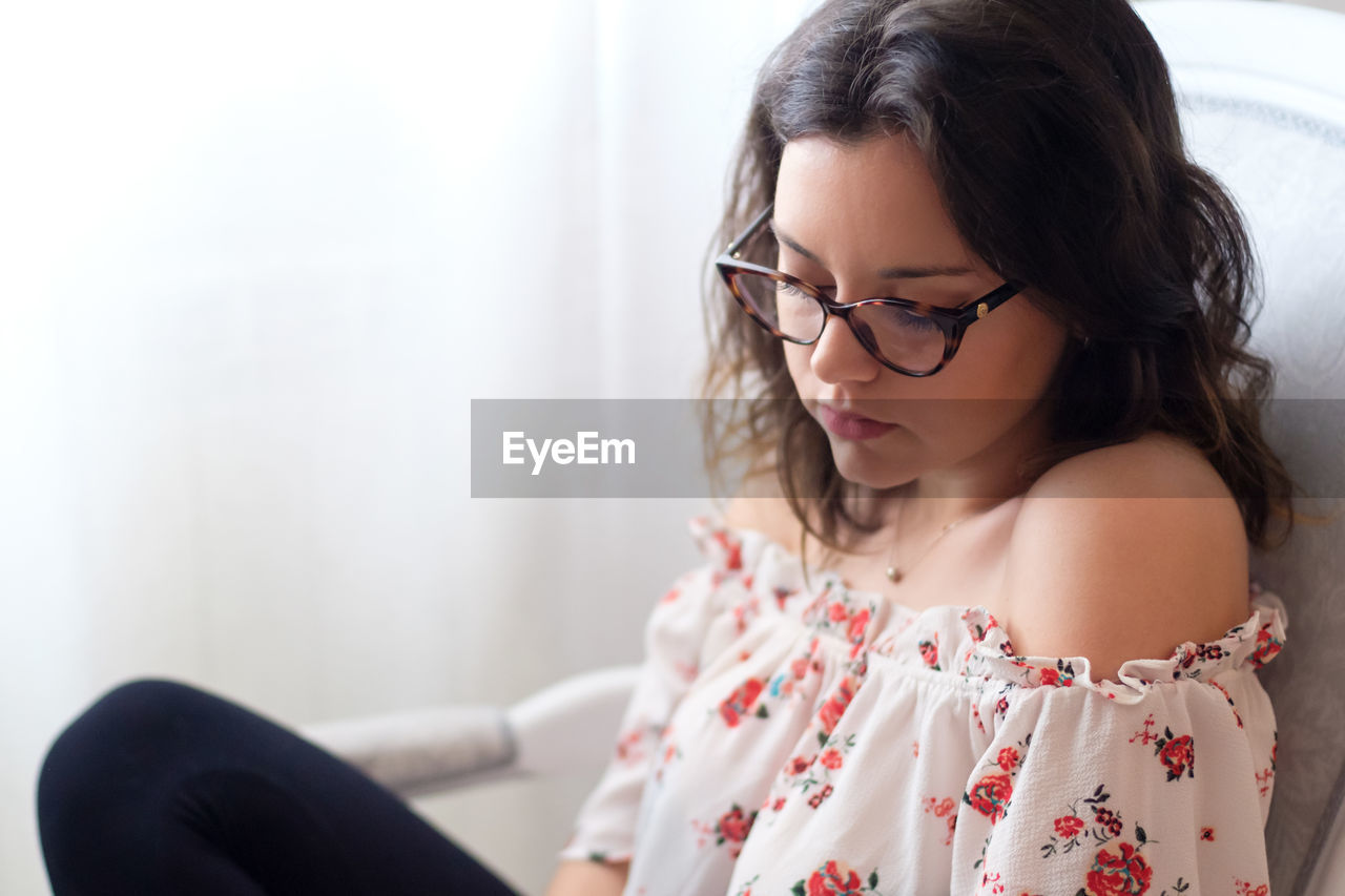 YOUNG WOMAN LOOKING AWAY WHILE SITTING ON TABLE