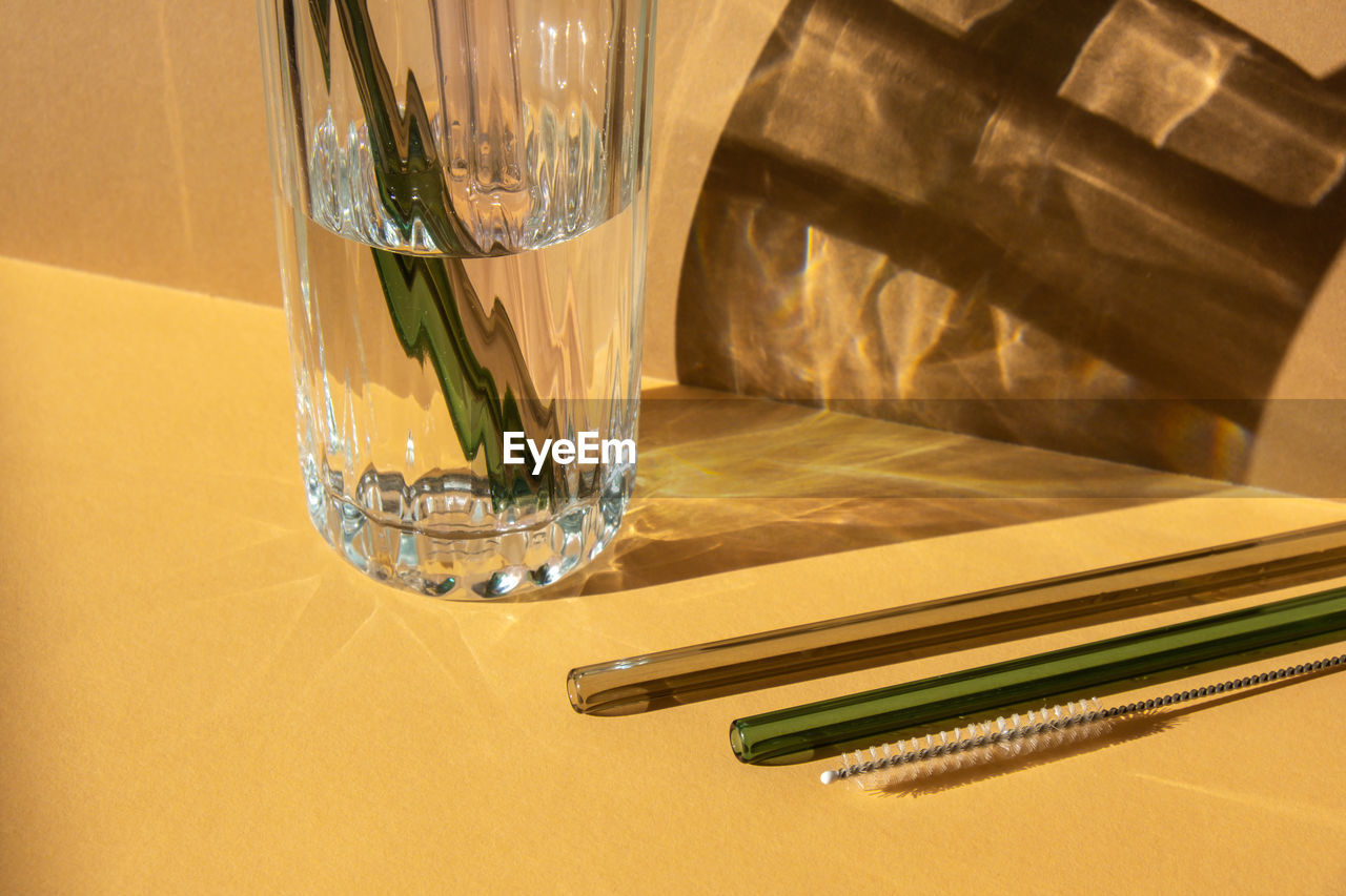 Reusable glass straws in glass with water on beige neutral background eco-friendly drinking straw