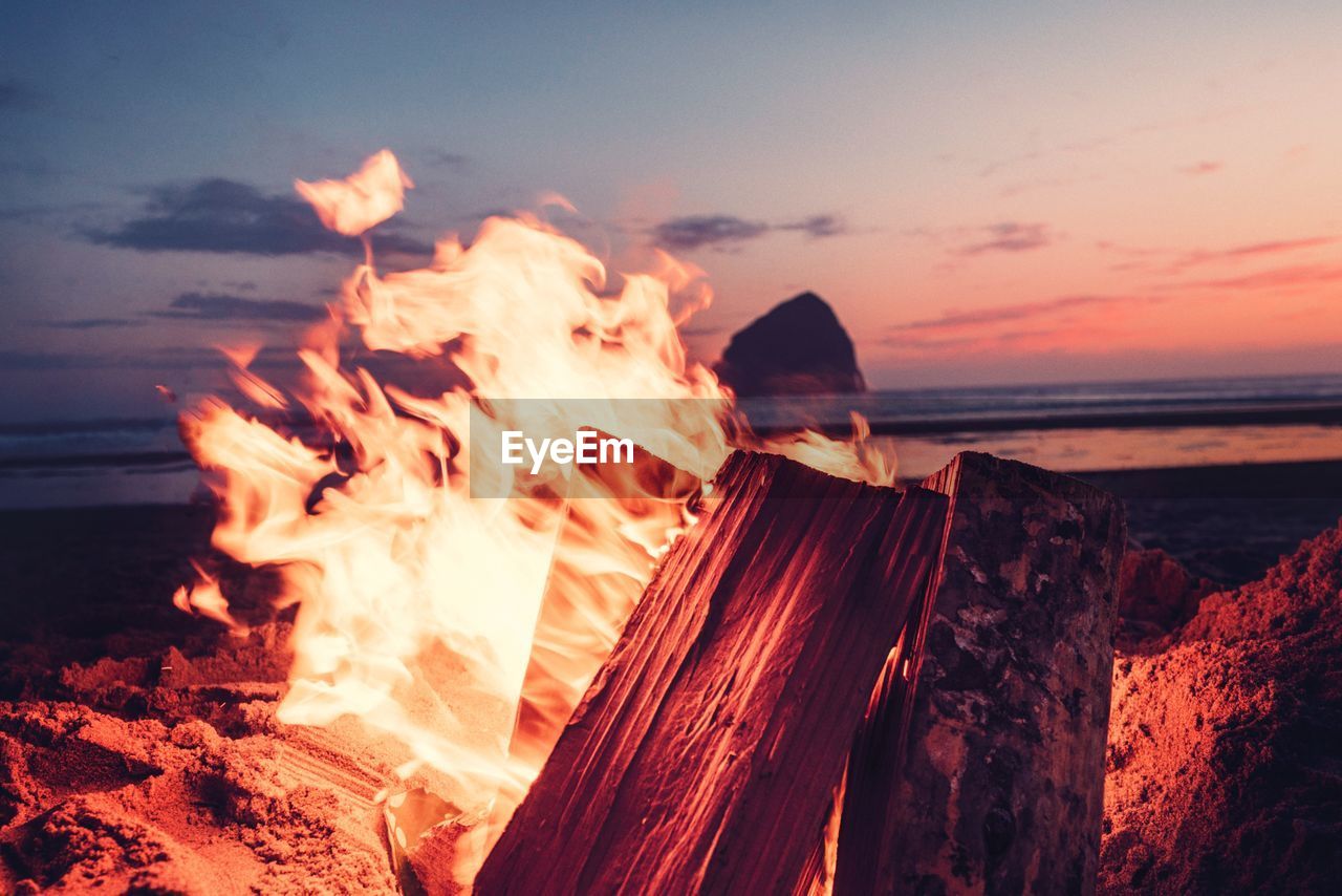 PANORAMIC VIEW OF BONFIRE ON SHORE AGAINST SUNSET