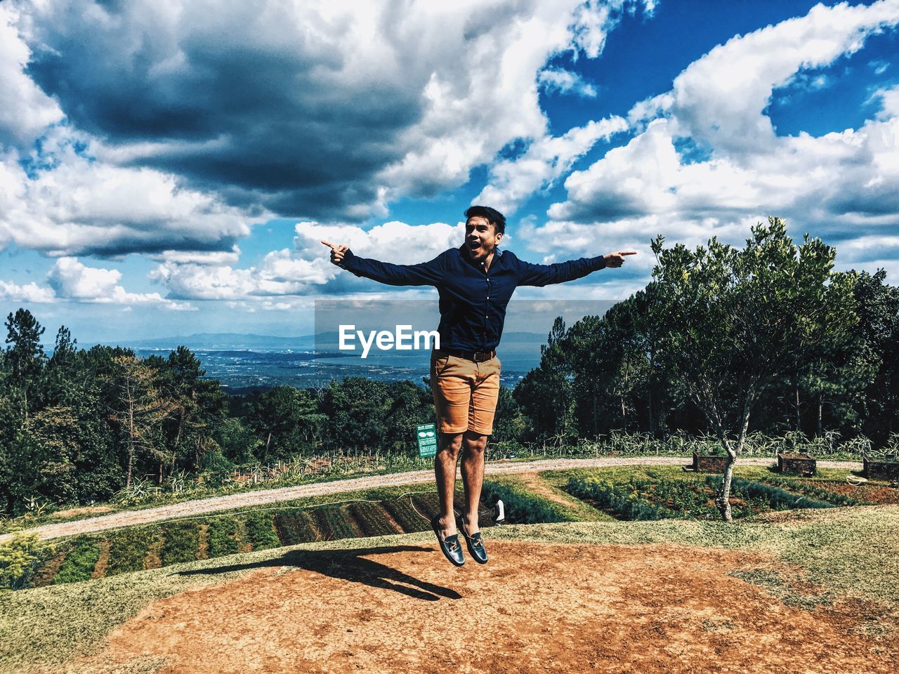 Young man jumping on field against cloudy sky