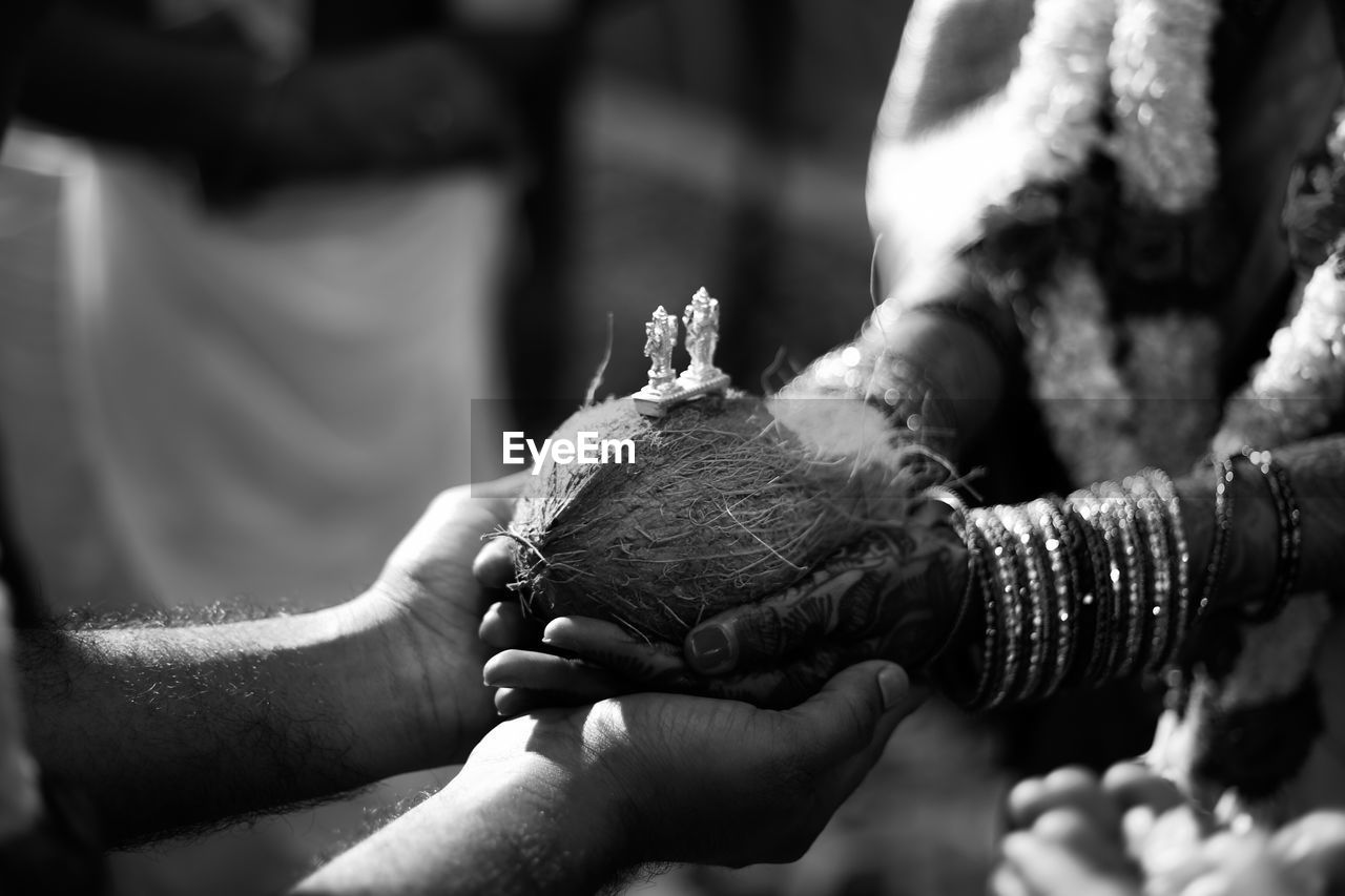 Cropped hands of couple holding coconut during wedding ceremony
