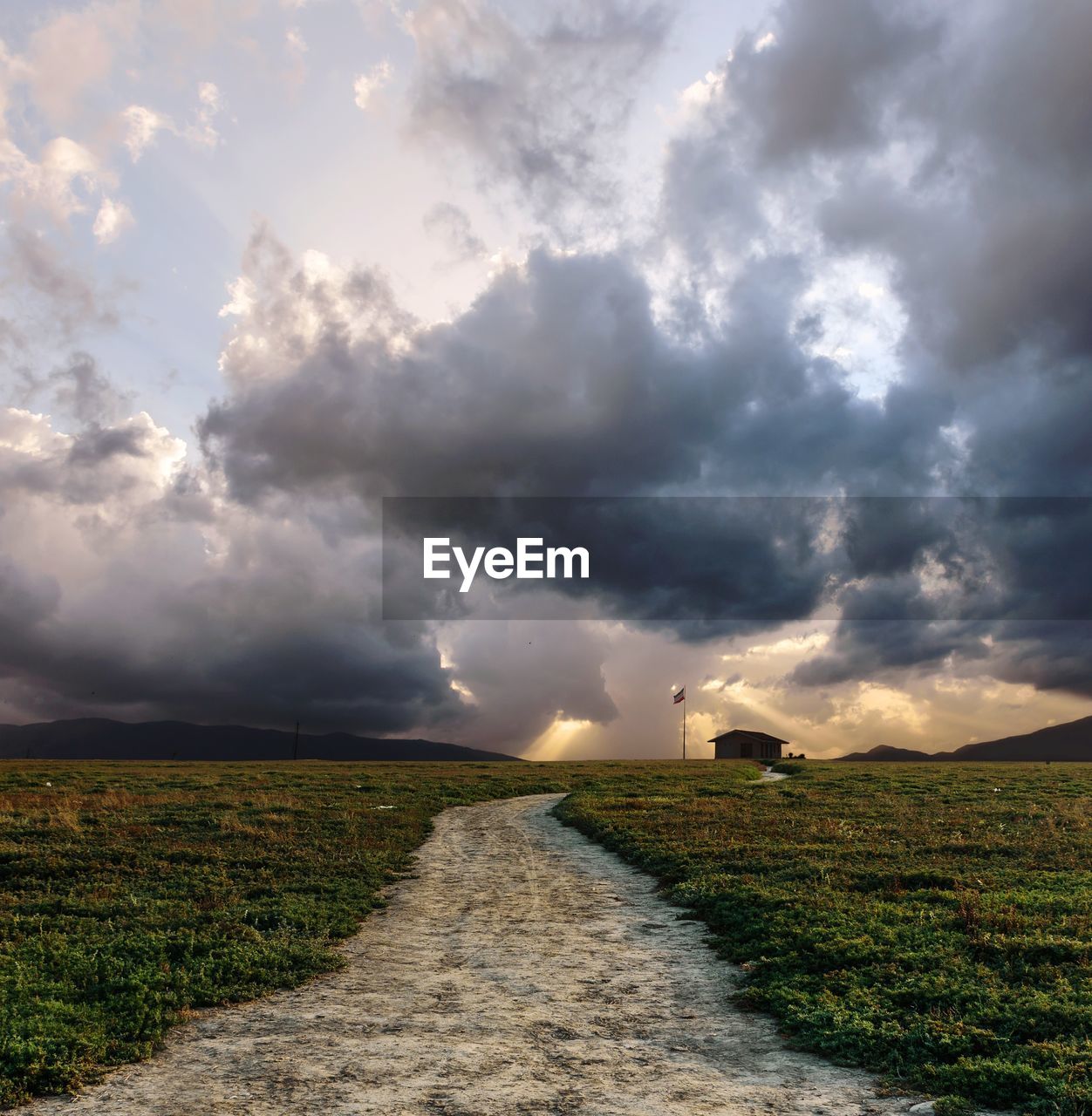 ROAD AMIDST FIELD AGAINST STORM CLOUDS