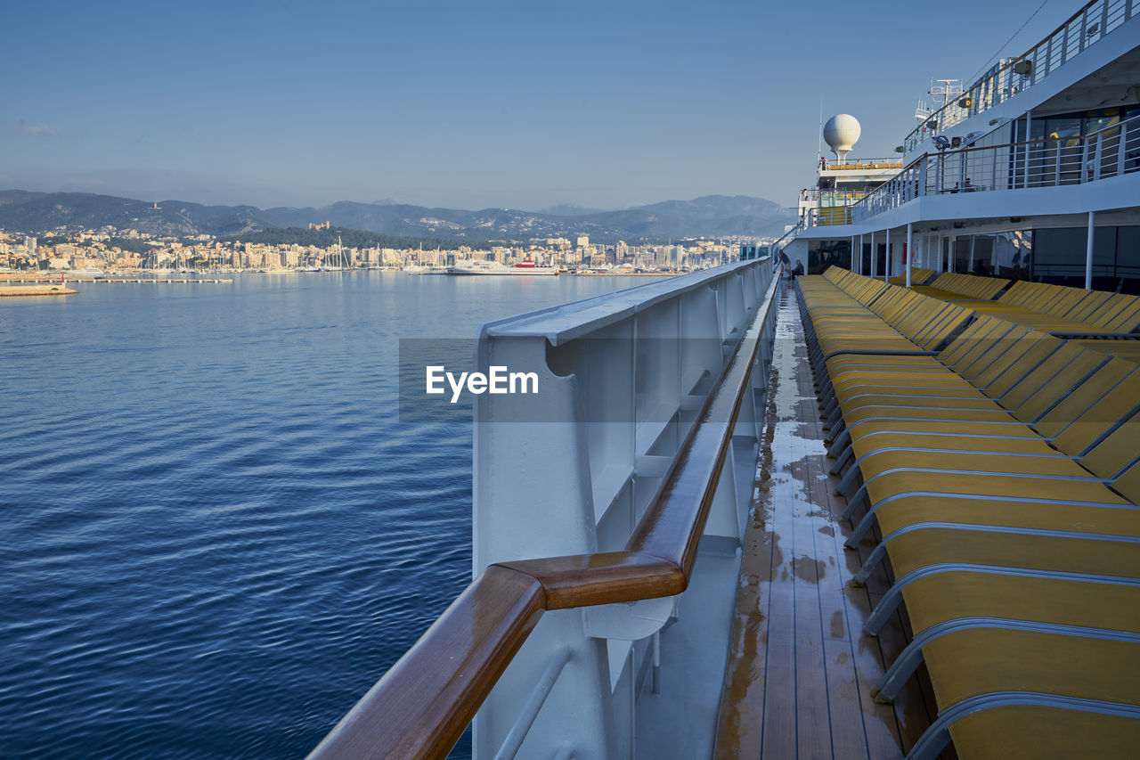 Close-up of chairs on boat in sea against buildings and sky