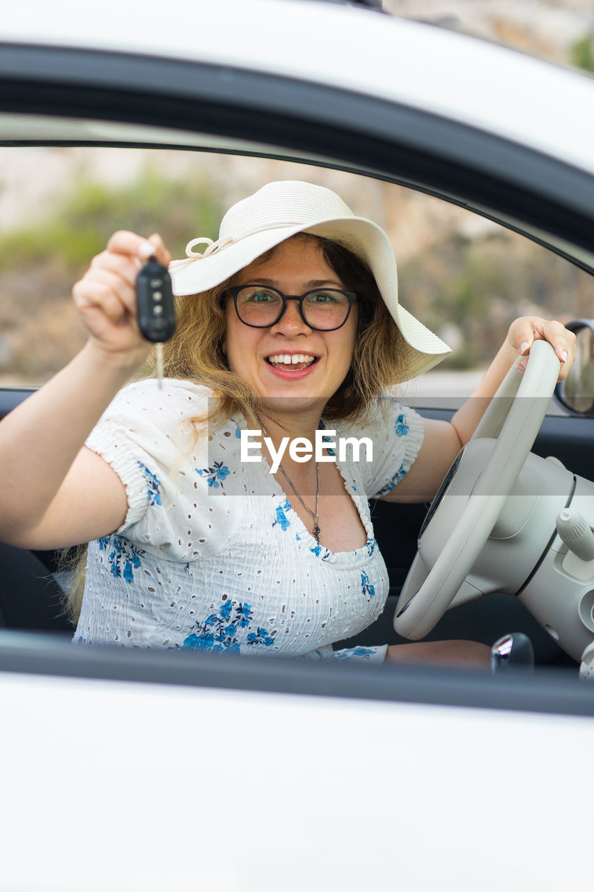 portrait of smiling young woman using mobile phone while sitting in car