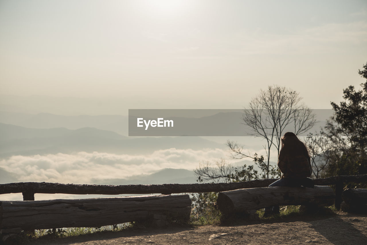 MAN SITTING ON LAKE AGAINST SKY